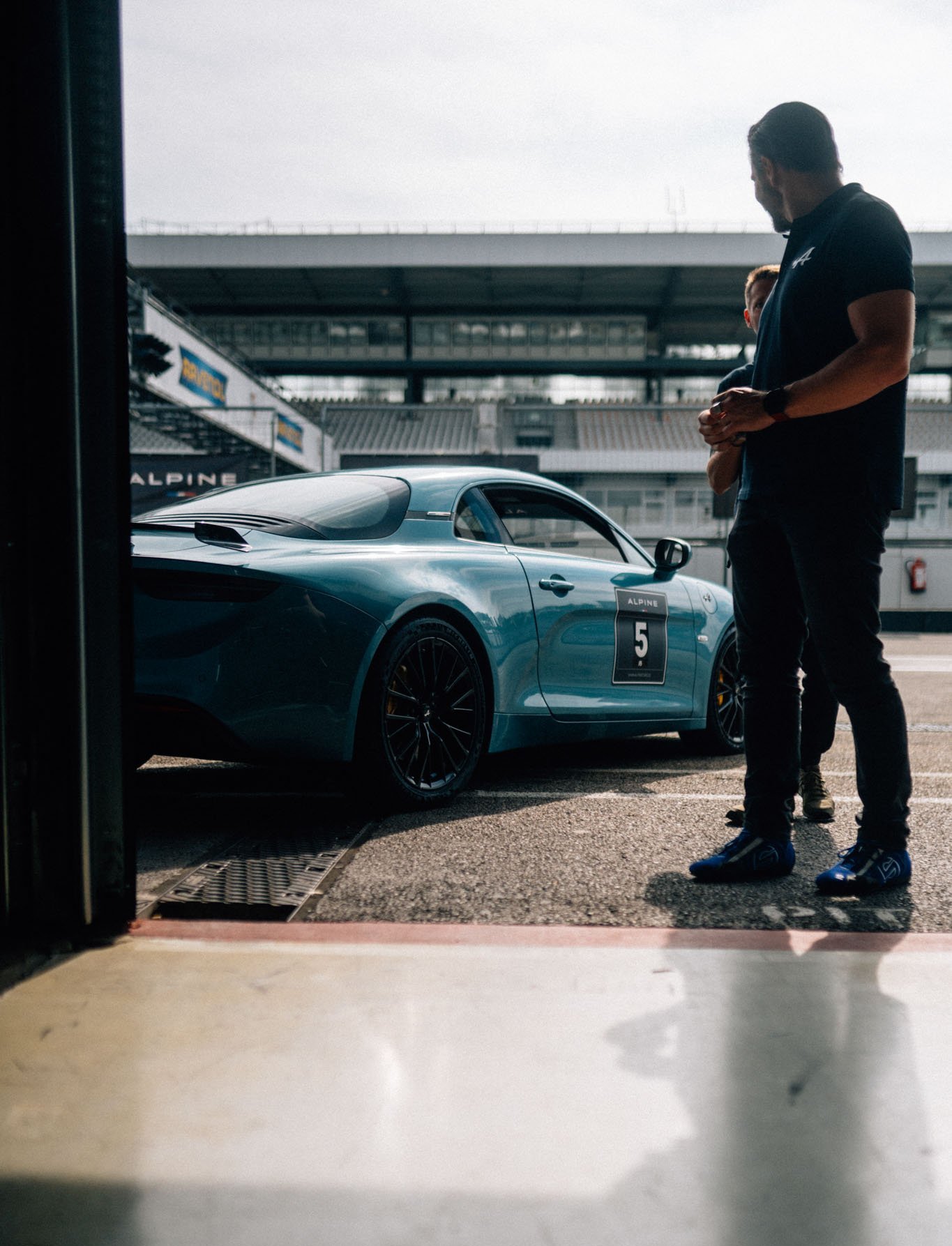 Alpine A110 die in der Boxengasse steht und aus der Pitbox fotografiert wurde. Ein Fahrer schaut sich sie an.